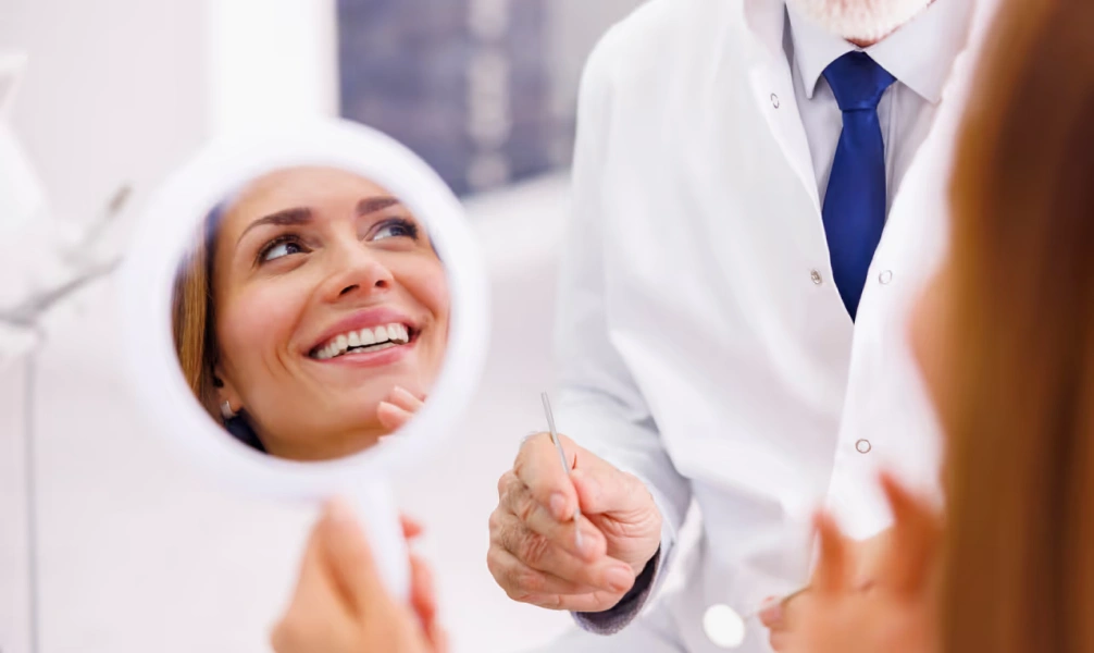 Patient smiling while viewing her restored smile in a dental mirror during a biomimetic dentistry appointment